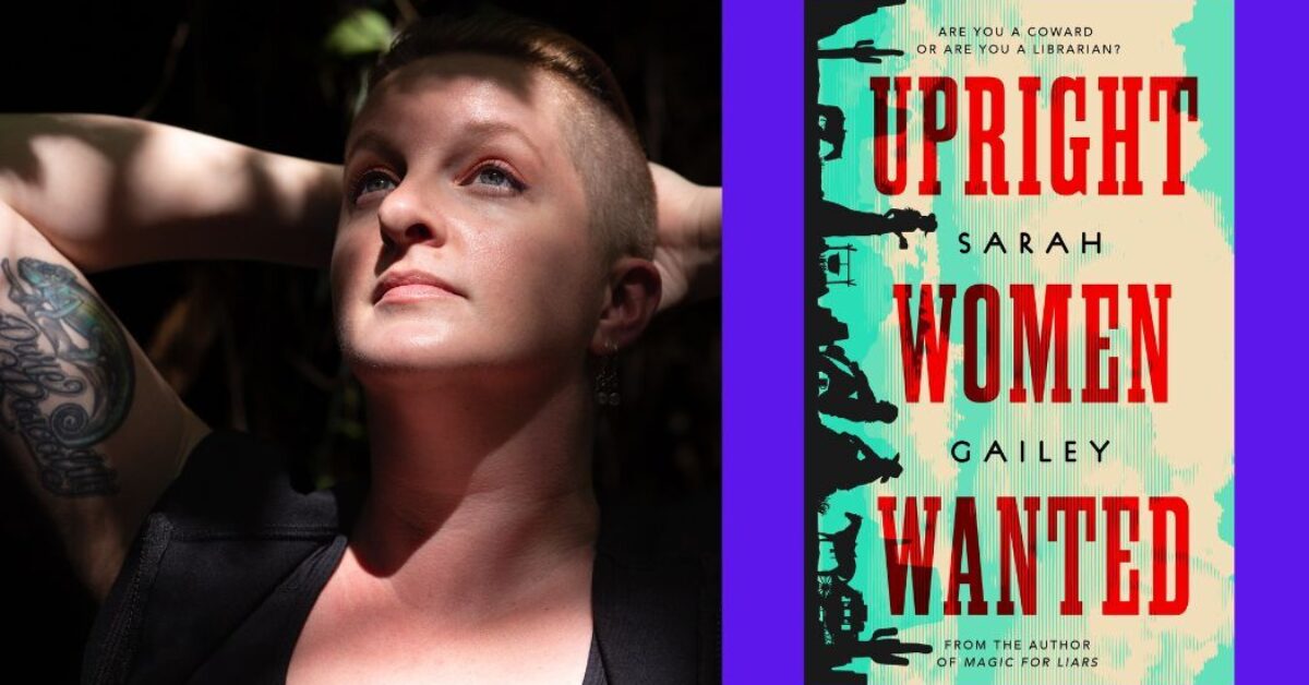 Sarah Gailey, a white person with auburn hair that is long on top and shaved on the sides, looking up with their hands behind their head. Dappled sun and shadow falls across their face, chest, and arms. Photo credit: ©Kate Dollarhyde 2023