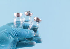 The Doctor's Gloved Hand Holds Vials Of Medicines On A Blue Back