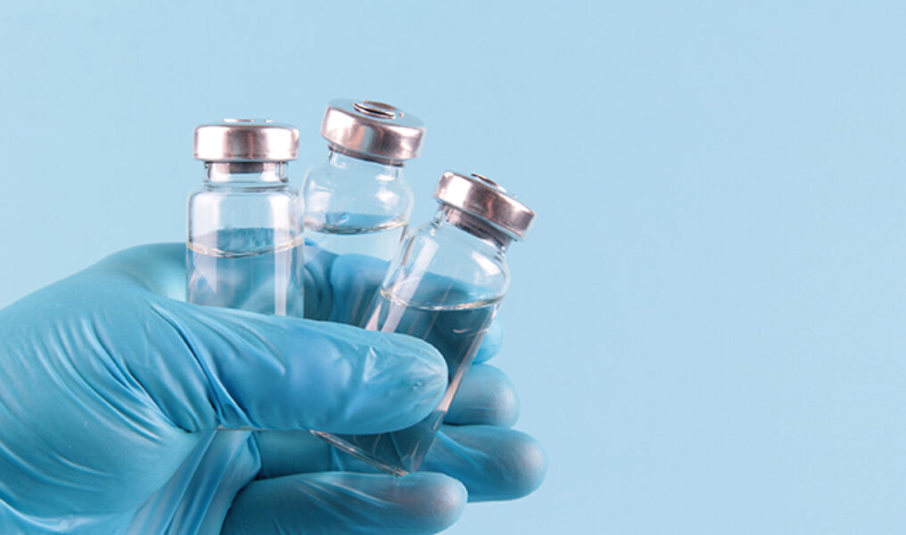 The Doctor's Gloved Hand Holds Vials Of Medicines On A Blue Back