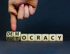 Democracy or autocracy symbol. Businessman turns wooden cubes and changes the word autocracy to democracy. Beautiful grey background, copy space. Business and democracy or autocracy concept.