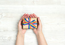 Female hands hold a gift box with rainbow LGBT ribbon on a light