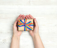 Female hands hold a gift box with rainbow LGBT ribbon on a light