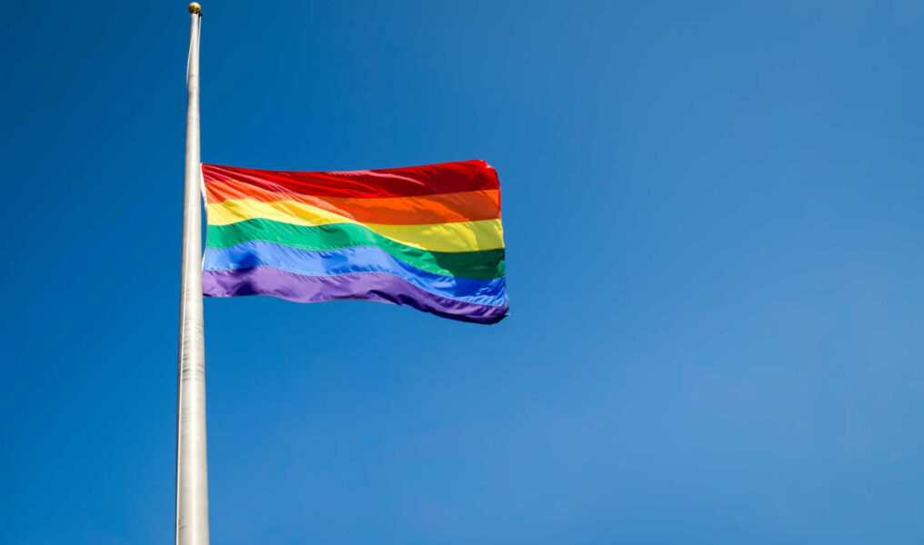 Gay pride rainbow flag flying at half mast in mourning on bright