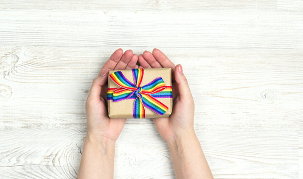Female hands hold a gift box with rainbow LGBT ribbon on a light