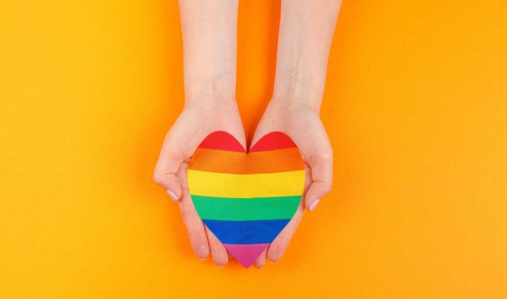 Gay Love. Human Hand Holding A Rainbow Paper Heart