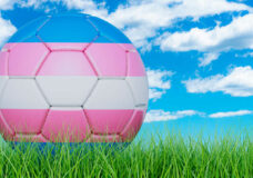 Soccer ball with transgender flag on the green grass against blu