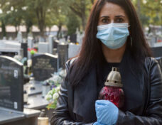 A woman wearing a protective mask against the coronavirus COVID-19 SARS-CoV-2 holds a candle in her hand and visits her relatives at the cemetery. Lockdown cemetery