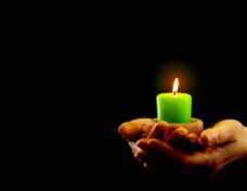 Hands Hold Green Burning Candle In The Dark.