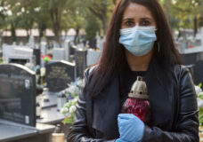 A woman wearing a protective mask against the coronavirus COVID-19 SARS-CoV-2 holds a candle in her hand and visits her relatives at the cemetery. Lockdown cemetery