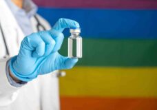 A Doctor Holding A Vaccine Bottle Against The Background Of The Rainbow Flag (lgbt). Vaccine For Imm