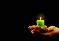 Hands Hold Green Burning Candle In The Dark.