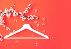 White wooden hanger hanging on the spring flowering branch on coral background. Spring sale concept discount store shopping empty hanger. Creative fashion beauty banner. Flat lay top view copy space.