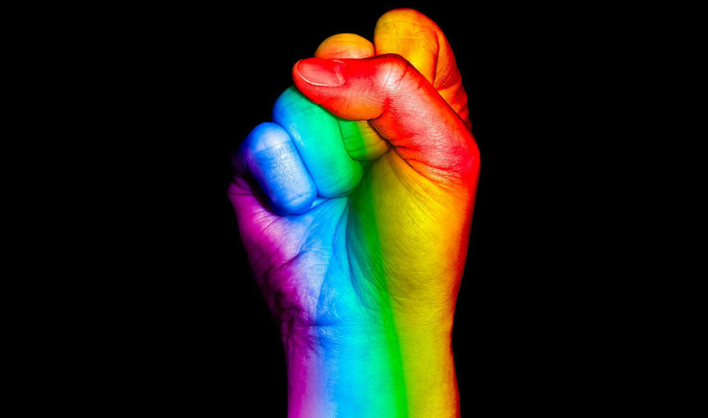 Fist Hand Symbol With Rainbow Flag Painted Raised On Black Background. Colorful Flag Sign Of Same-se