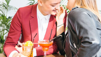 Crop young girlfriends sitting with cocktails at table and enjoying each other.