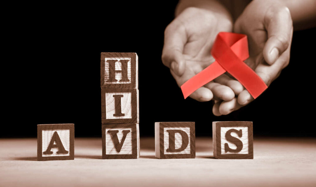 Hand holding red ribbon on back of HIV-AIDS letter blocks