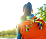girl student wears backpack outdoors in summer park