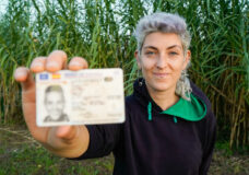 non-binary person looking at camera with ID in hand. non-binary